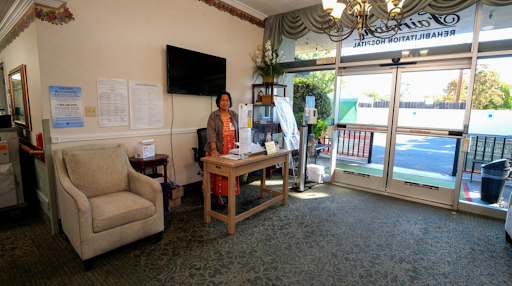 A welcoming lobby with a woman standing behind a table, adorned with plants and soft furniture.
