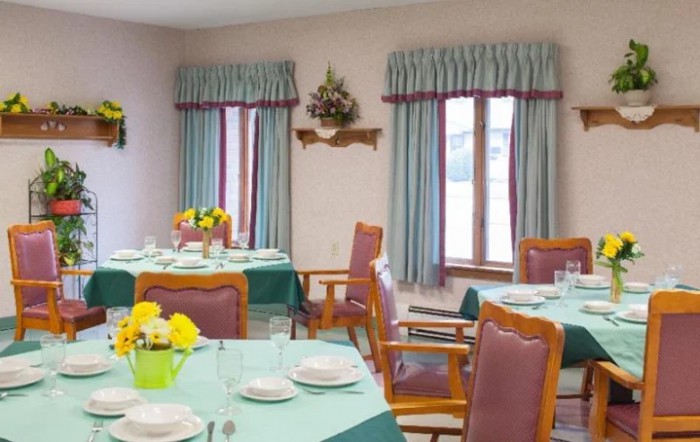 A neatly arranged dining area with tables set, featuring colorful flowers and large windows with curtains.