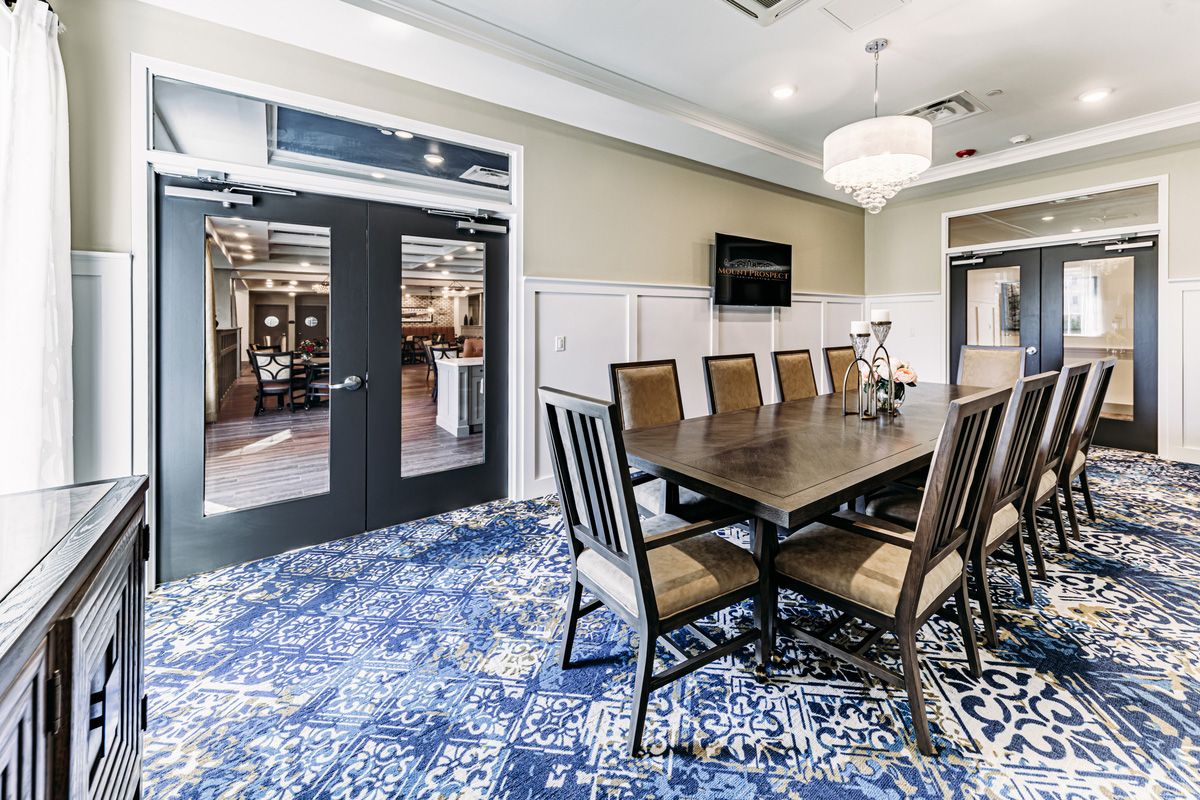 A modern dining or conference room featuring a large table with several chairs, elegant lighting, and a patterned carpet.