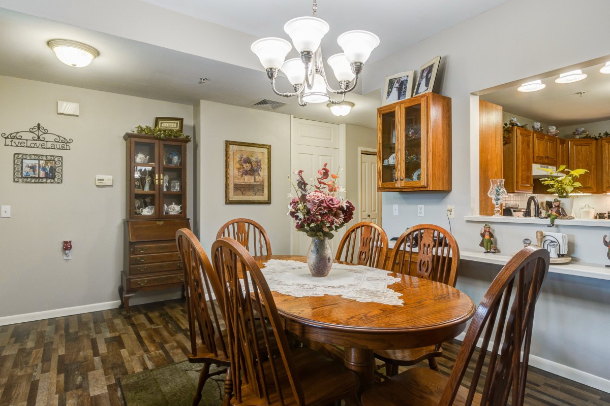 A cozy dining room with a wooden table and chairs, adorned with a decorative centerpiece under a chandelier.