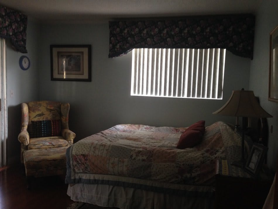 A cozy bedroom with a bed, armchair, and window blinds.