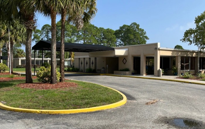 A building with a driveway and surrounding palm trees on a sunny day.
