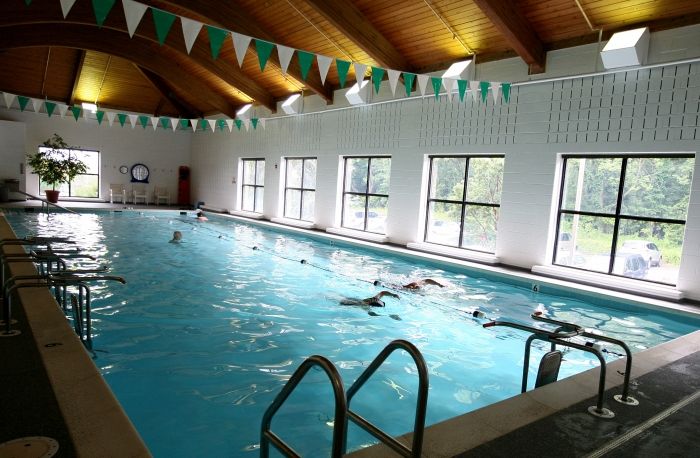 People swimming in an indoor pool with wooden ceiling and natural light.