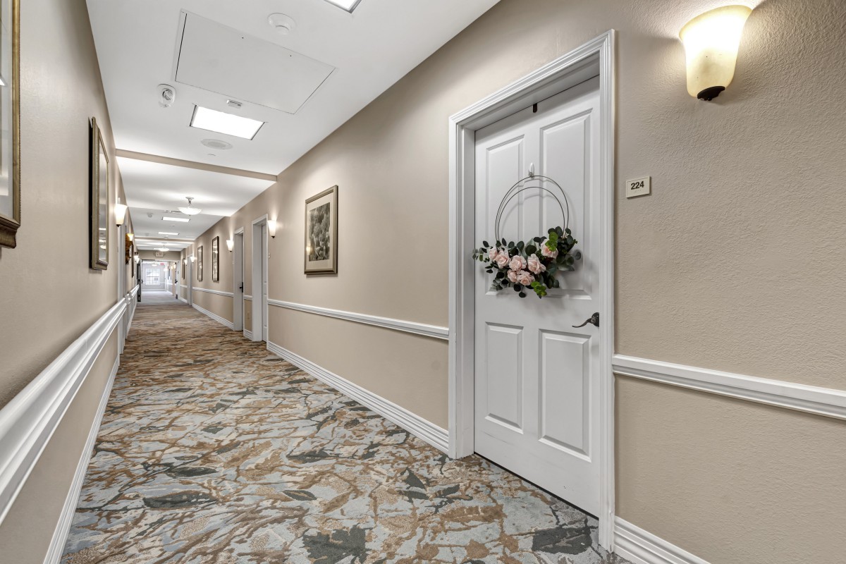 A decorated hallway with carpet and wall art, featuring a door adorned with a floral wreath.