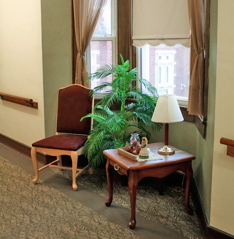 A cozy corner featuring a chair, side table with a lamp, and a plant by the window.