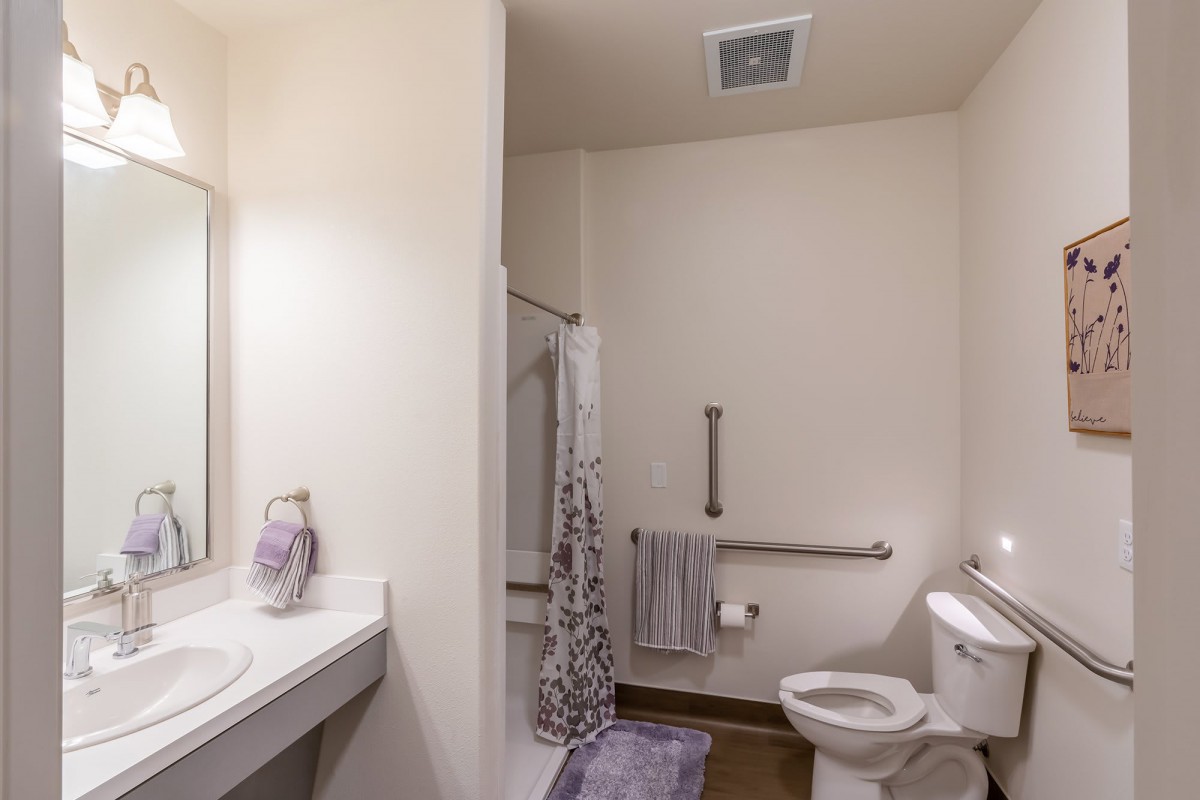 A bathroom featuring a sink, toilet, shower area with curtain, and accessories like towels and a bath mat.