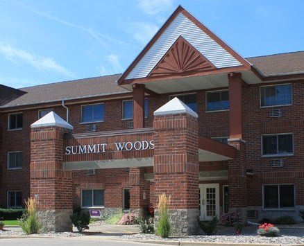 The front entrance of the Summit Woods residential building, featuring a brick facade and peaked roof design.