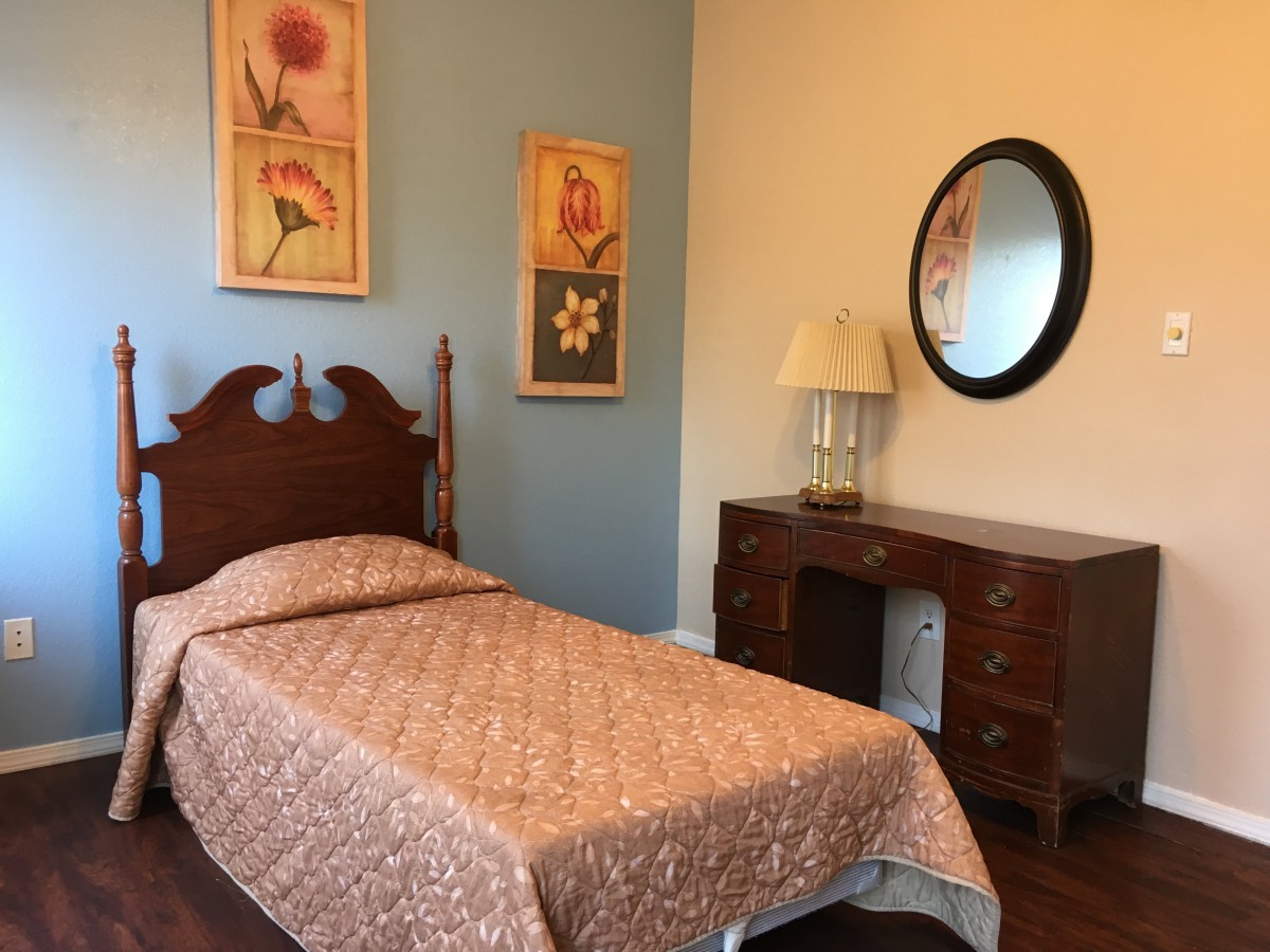 A cozy bedroom with a single bed, wooden furniture, and decorative floral art on the walls.