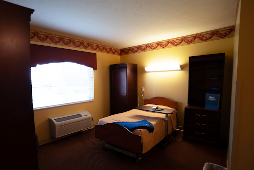 A simple hotel room featuring a bed, a window with curtains, and basic furniture.