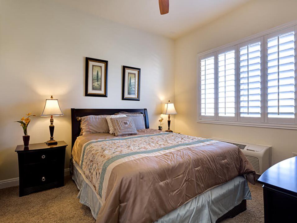A cozy bedroom with a neatly made bed, flanked by two lamps and decorative wall art.