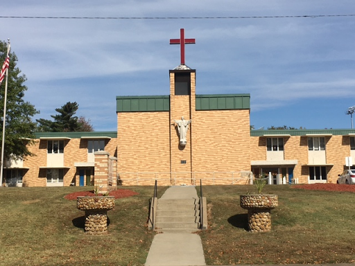 A church building featuring a prominent cross on top, surrounded by landscaped grass.