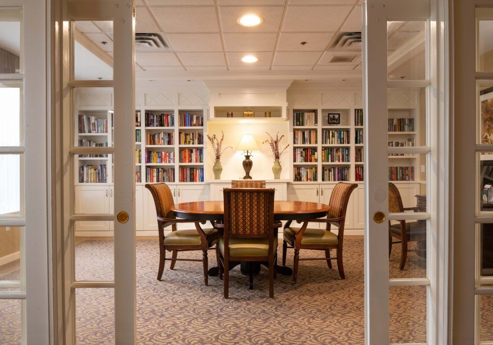 An elegant library with a wooden table and chairs, surrounded by bookshelves.
