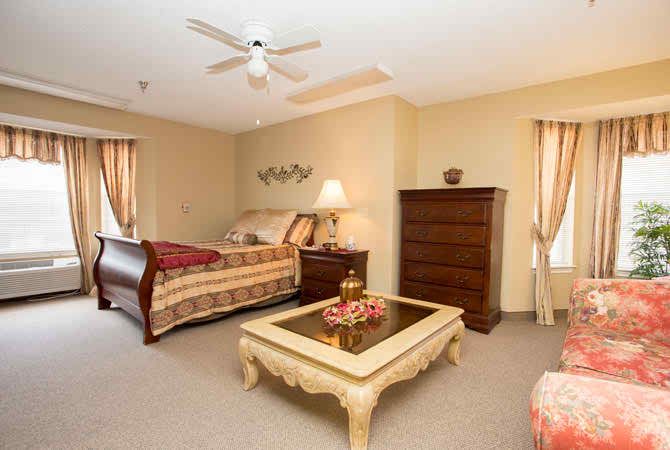 A spacious bedroom with a large bed, a dresser, and a coffee table under warm lighting.