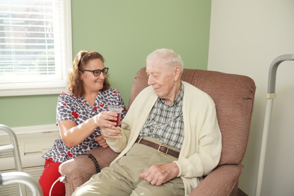 A caregiver assists an elderly man in a comfortable home setting.