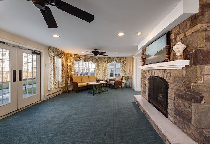 A cozy living room with a fireplace, carpeted floor, and multiple windows.