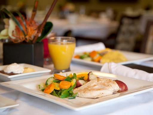A delicious breakfast featuring grilled chicken, fresh salad, and a glass of orange juice.