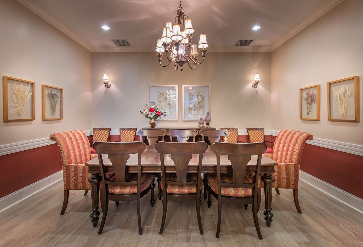 An elegant dining room with a long table, upholstered chairs, and a chandelier overhead.