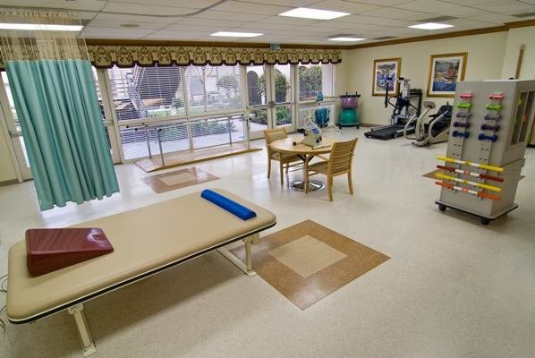 A well-equipped physical therapy and rehabilitation room with exercise machines and a treatment table.