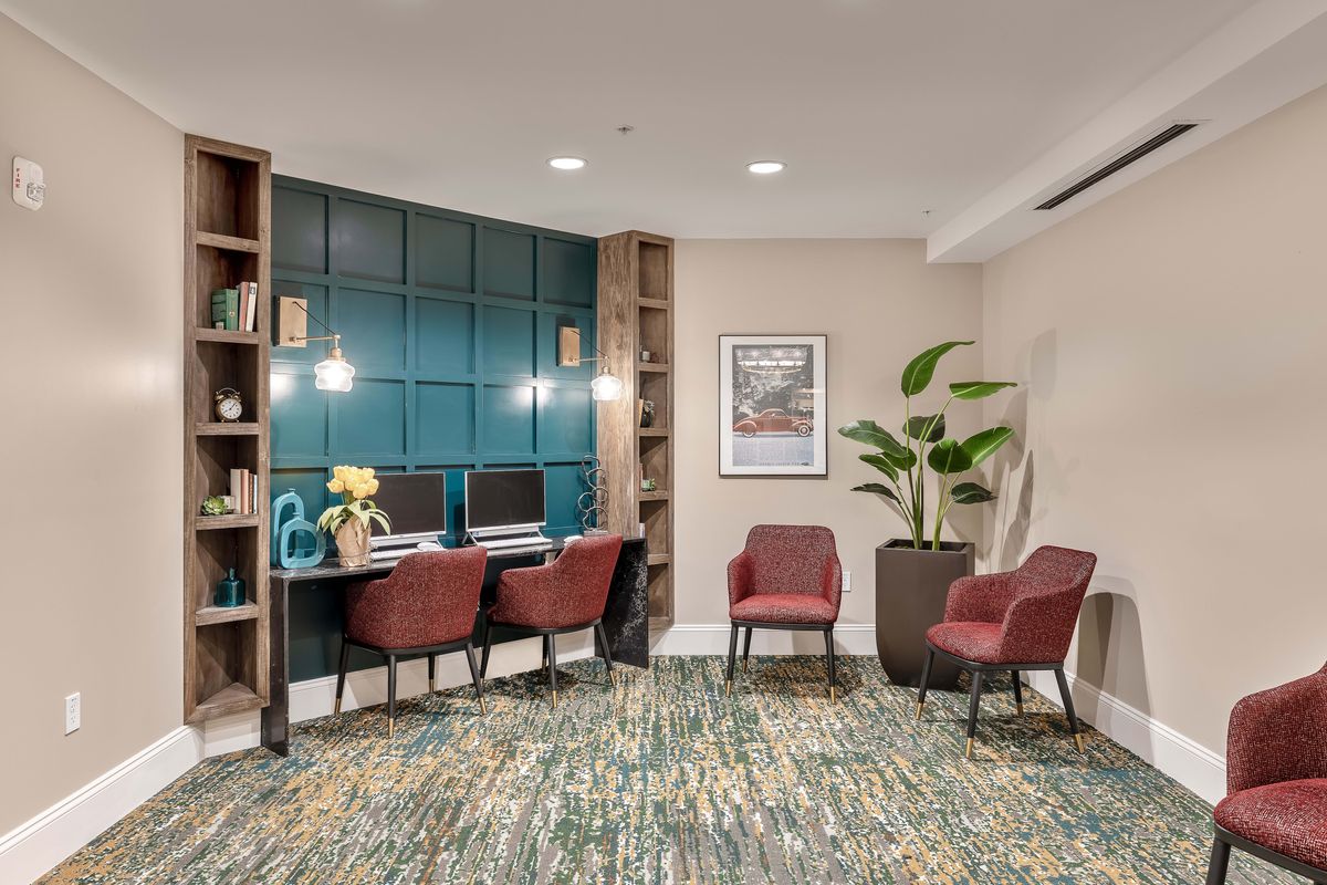 A cozy office workspace featuring two computer stations with red chairs, a patterned carpet, decorative wall paneling, and indoor plants for a welcoming atmosphere.