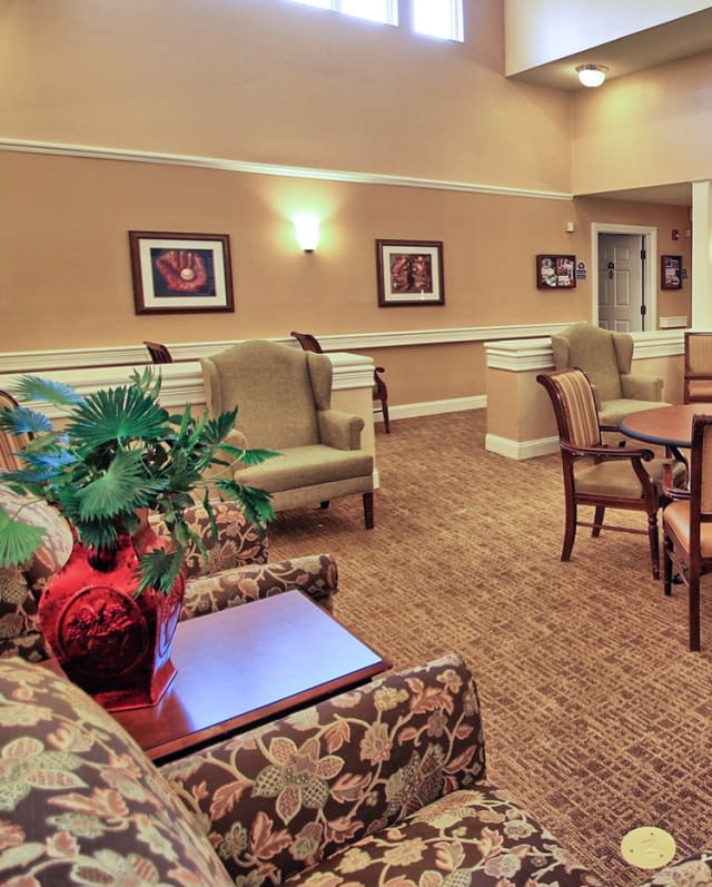A cozy seating area with comfortable chairs and a table, decorated with paintings and plants.