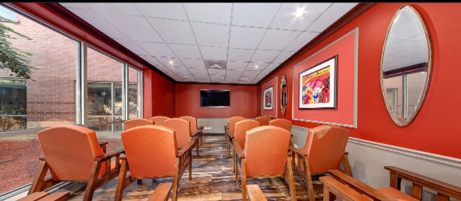 A small conference room with rows of chairs facing a television, adorned with colorful artwork on the walls.
