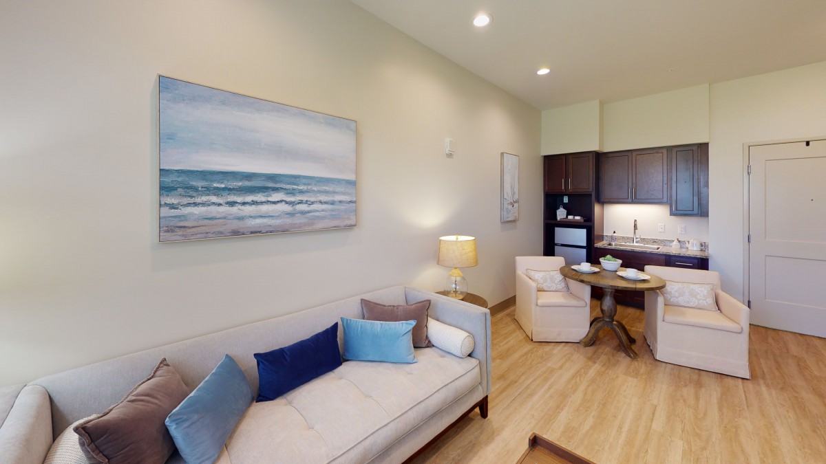 A modern and cozy living room with a sofa, artwork on the wall, and an adjoining kitchen area.