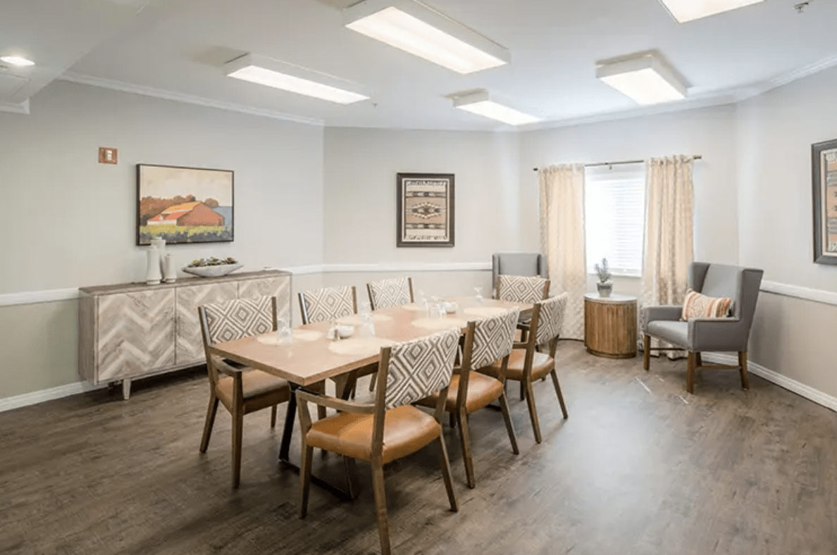 A modern dining room with a large wooden table, comfortable chairs, and wall art under soft lighting.