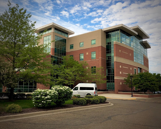 A modern office building surrounded by lush greenery under a partly cloudy sky.