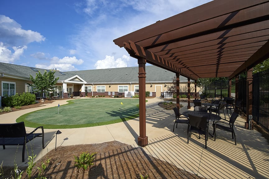 A sunny outdoor area with a pergola, seating, and a well-maintained lawn in front of a building.