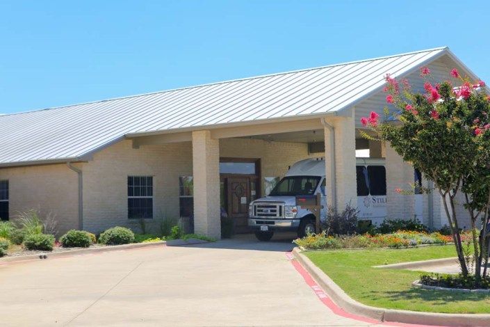 A building entrance with a bus parked under an awning on a sunny day.