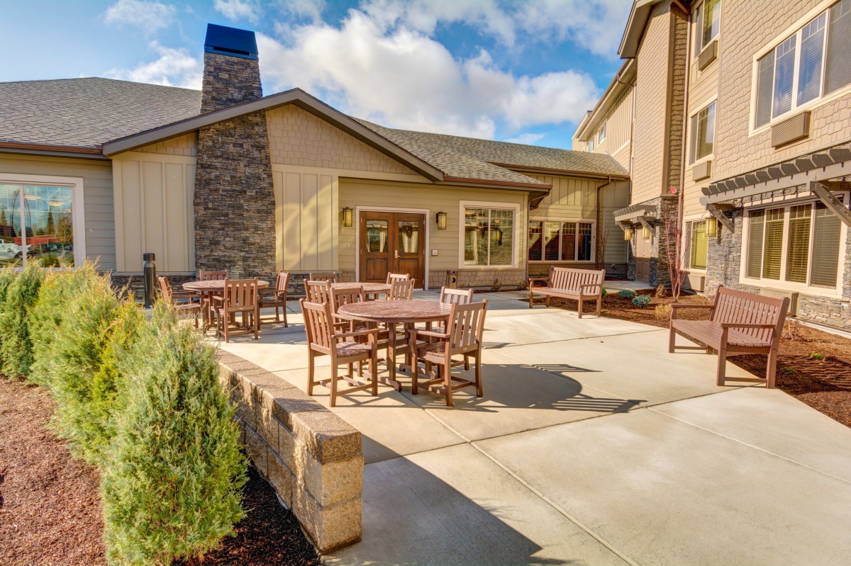 Outdoor patio with tables and chairs in front of a building under a partly cloudy sky.