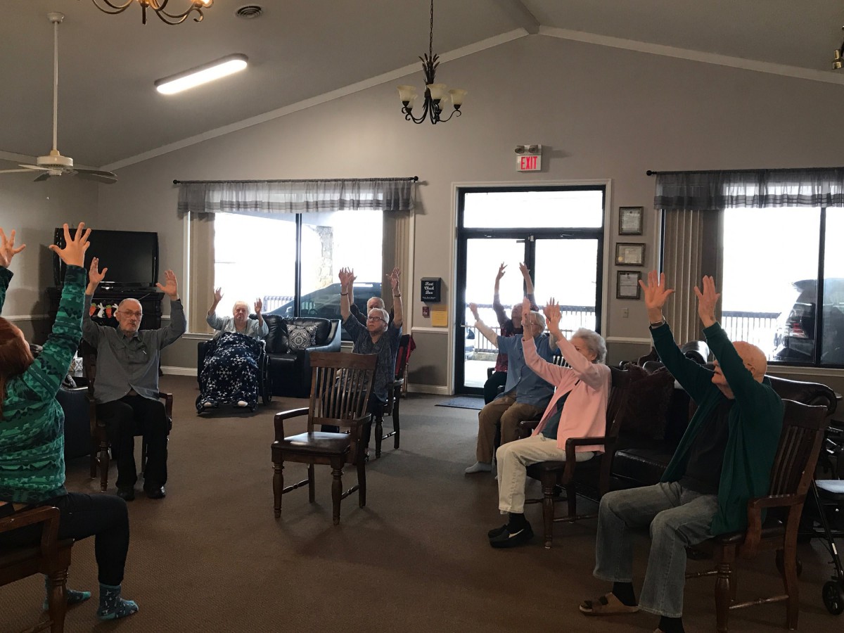 A group of elderly people participating in a seated exercise session indoors.