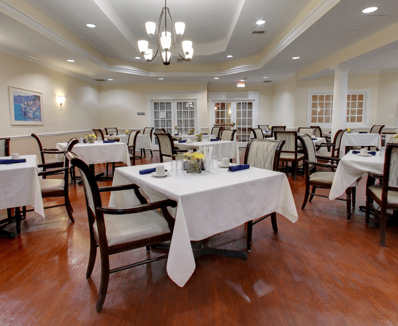 An elegant dining area with neatly arranged tables and chairs, featuring chandeliers for ambient lighting.