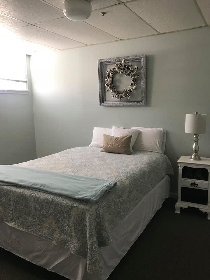 A minimalist bedroom with a neatly made bed, a nightstand with a lamp, and wall decor.