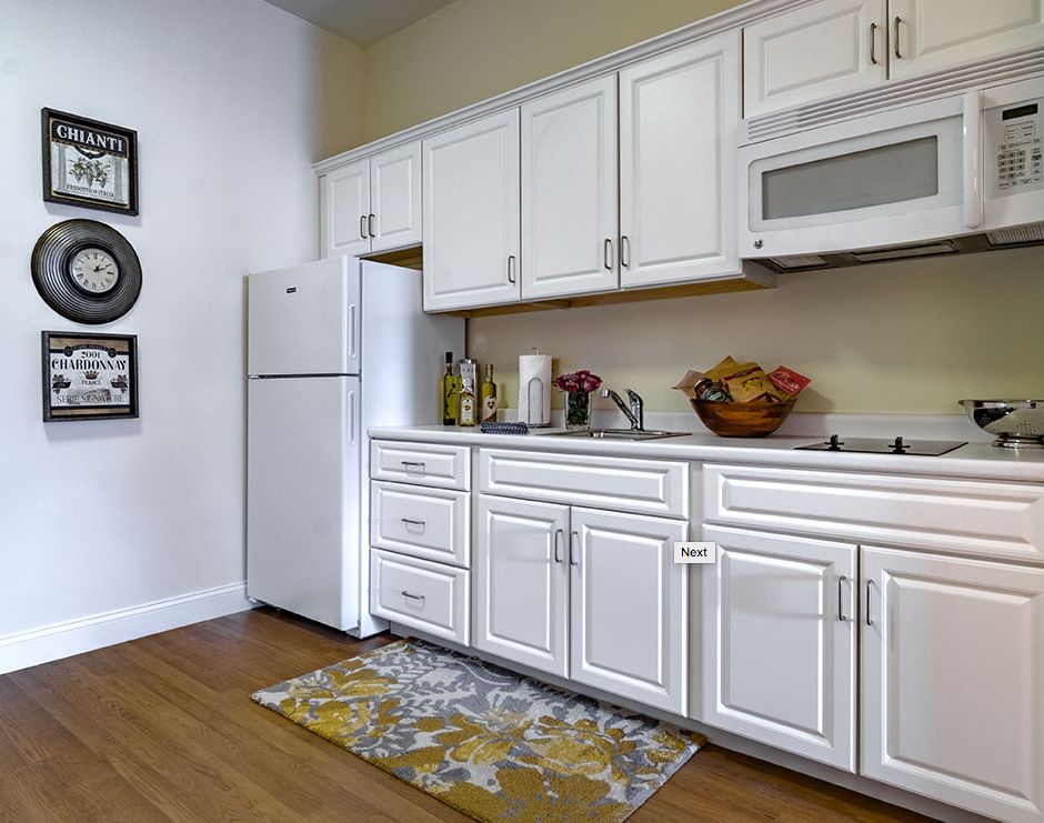 A modern kitchen with white cabinets, appliances, and a decorative rug on wooden flooring.