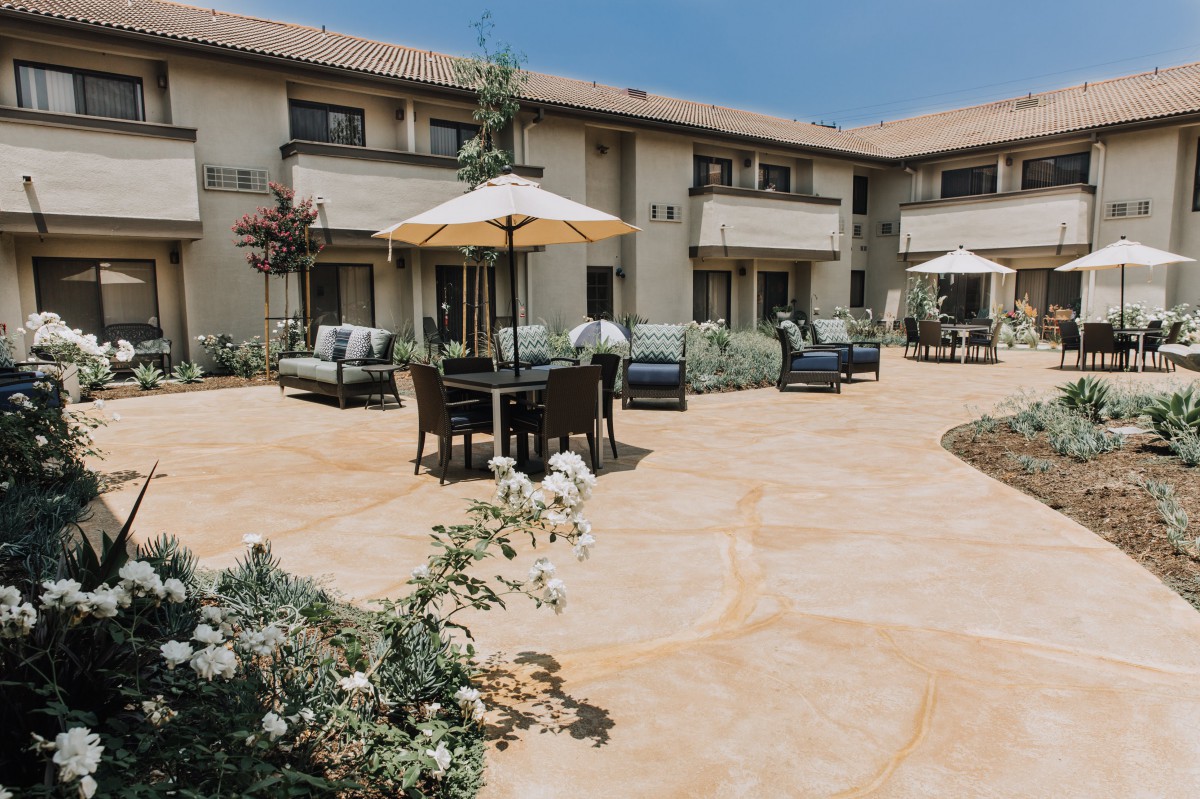 A sunny patio area with outdoor furniture and umbrellas in front of a residential building.