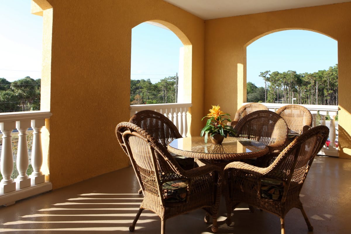 A sunlit patio with wicker furniture and a flower vase on the table.