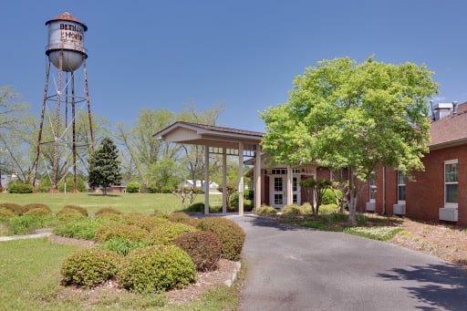 A building entrance with a driveway, surrounded by trees and bushes, next to a water tower.