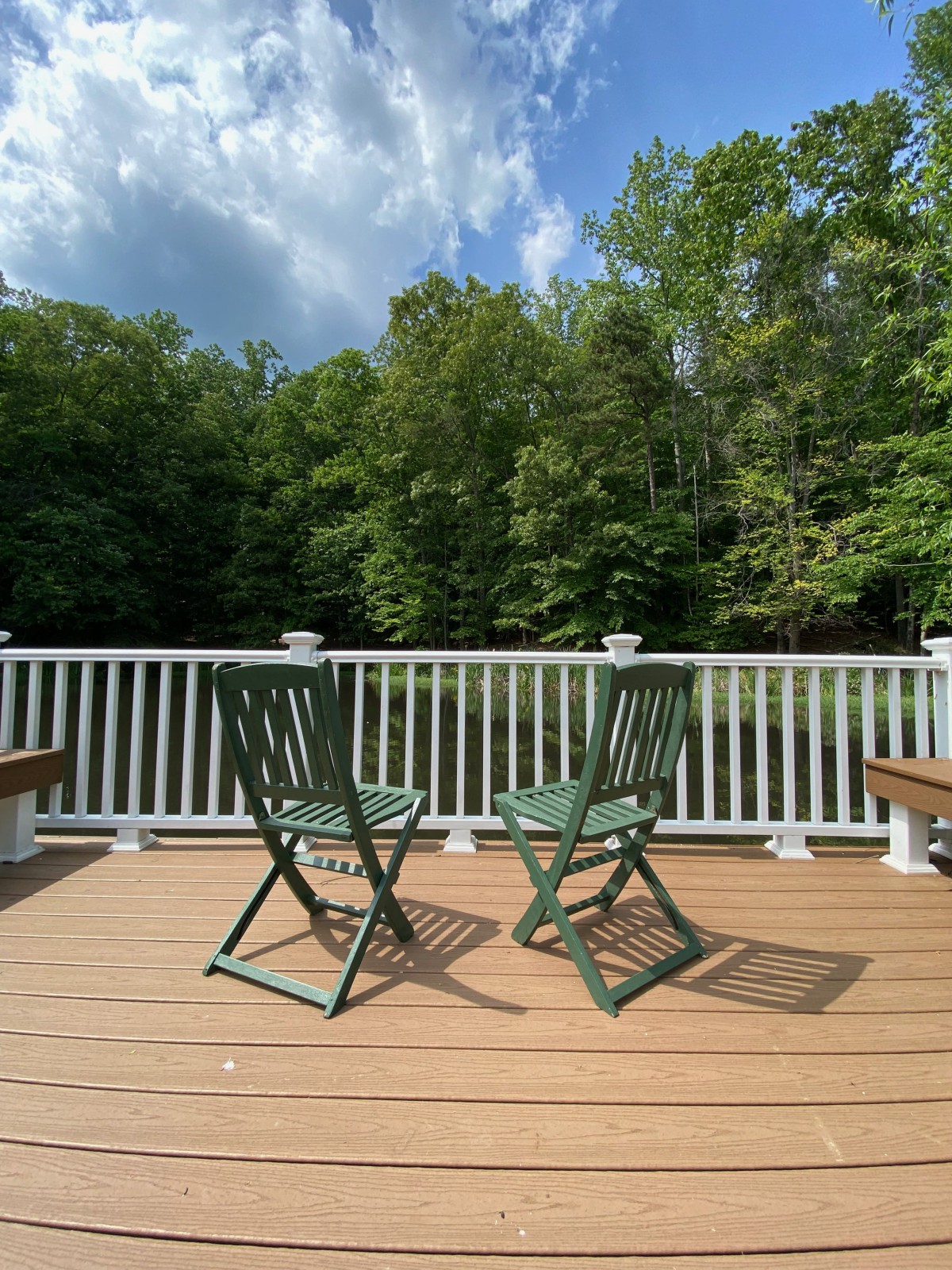A tranquil deck featuring two green chairs facing a lush forest backdrop under a clear blue sky.