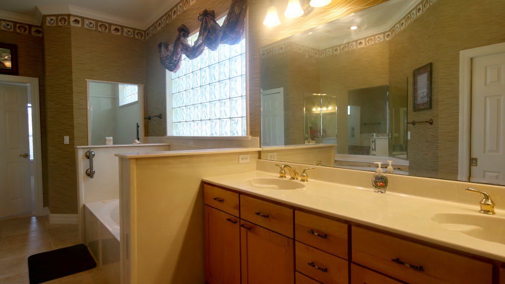 A spacious bathroom with a large vanity and mirror, featuring warm lighting and elegant cabinetry.