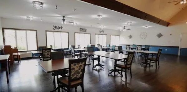 A spacious dining room with several arranged tables and chairs, well-lit by natural light from multiple windows.