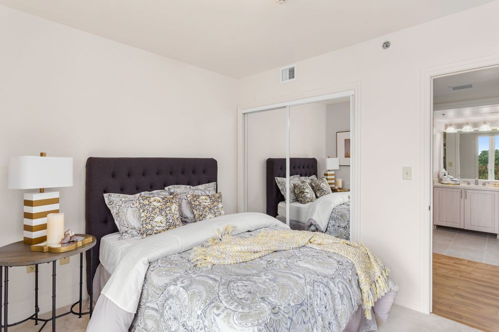 A cozy bedroom with a neatly made bed, decorative pillows, and a mirrored closet.