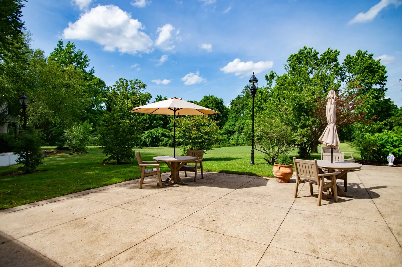 A peaceful backyard patio with outdoor furniture and an umbrella, surrounded by lush greenery.