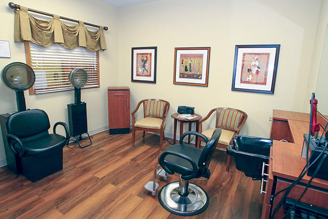 A cozy hair salon interior with wooden floors, stylish chairs, and framed artwork on the walls.