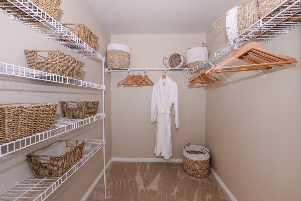 A neatly organized walk-in closet featuring shelves with baskets, hangers, and a robe.