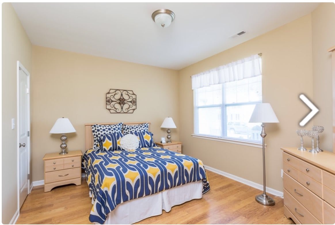 A cozy bedroom with a colorful bedspread, two bedside tables with lamps, and a large window providing natural light.