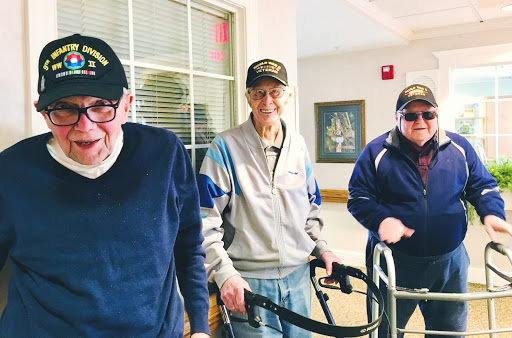 Three smiling veterans enjoying a moment together indoors, equipped with walking aids.
