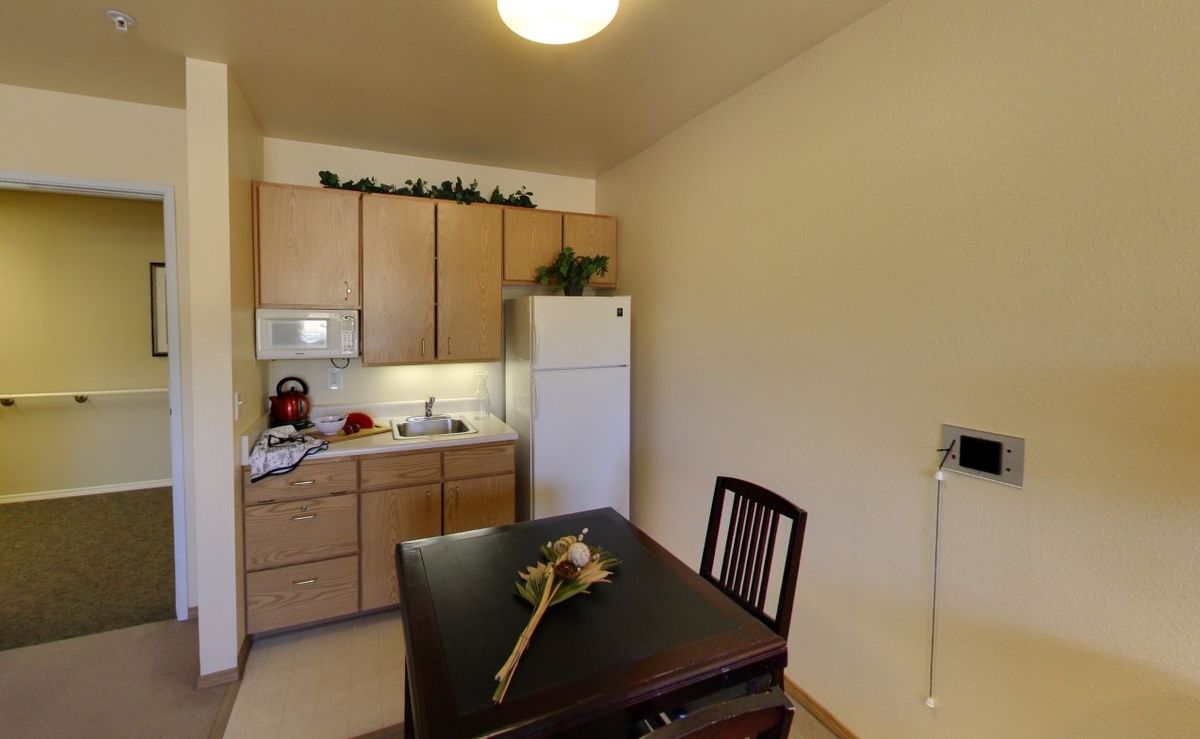 A small kitchen with a dining area, featuring a refrigerator, cabinets, and a microwave.