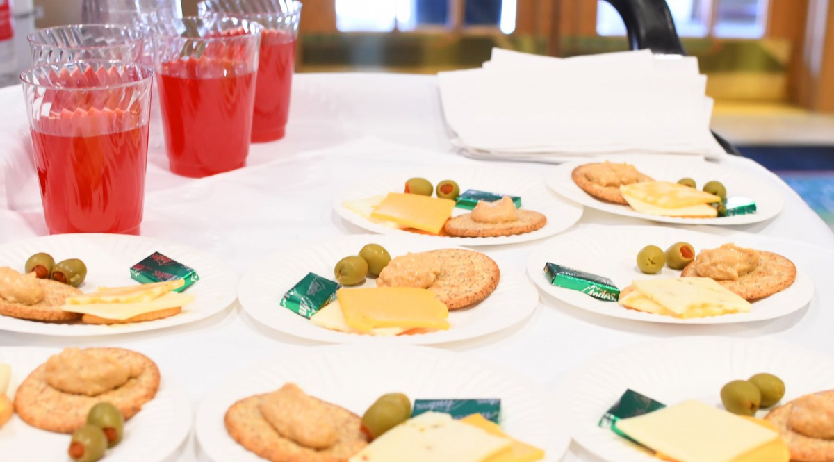 Plates of snacks with cheese, crackers, and olives, accompanied by red drinks.