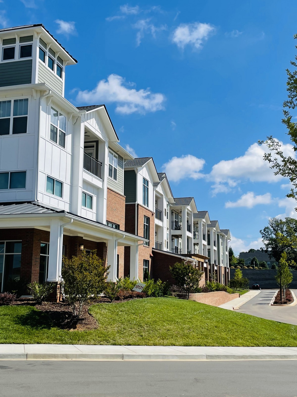 A row of modern suburban apartment buildings with a well-maintained lawn and a clear blue sky.